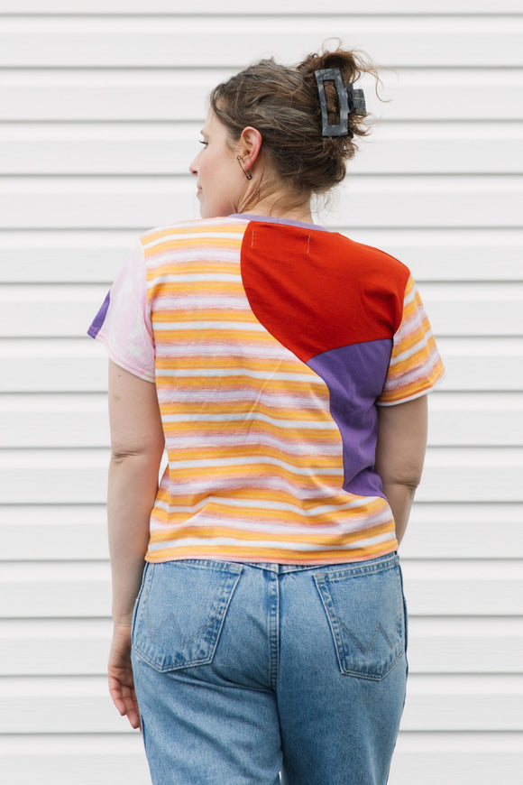Person wearing a colorful striped shirt and blue jeans against a white wall.