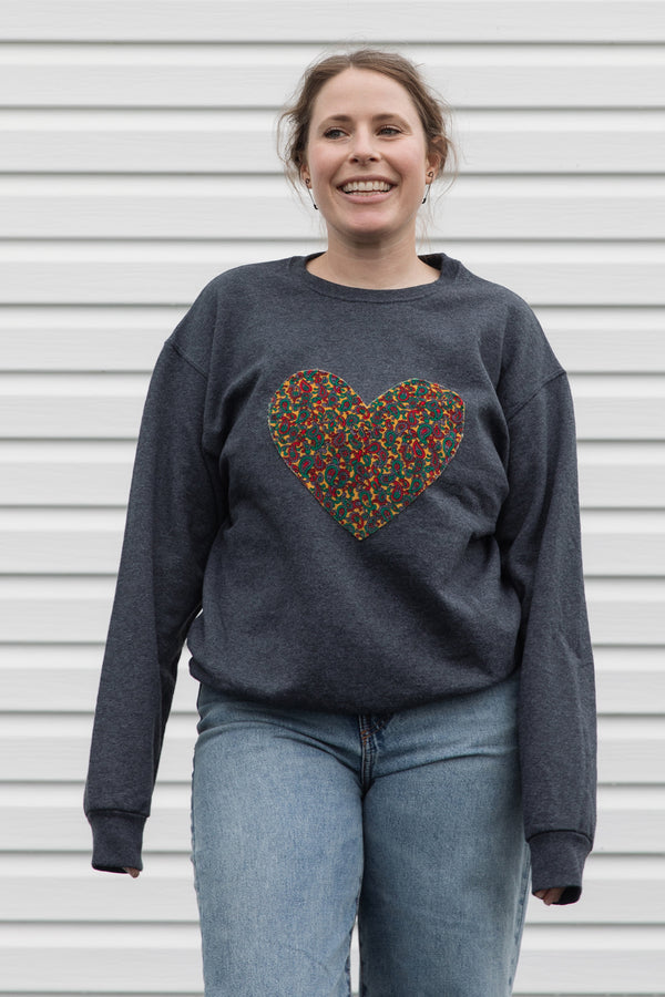 Woman wearing a dark gray sweatshirt with a colorful heart design sewn in canada