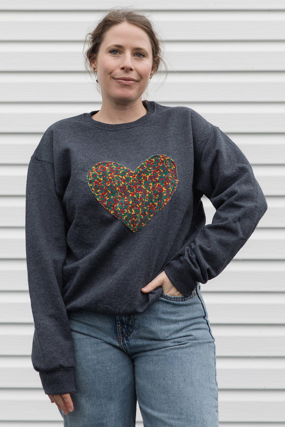 Woman wearing a dark gray sweatshirt with a colorful heart design sewn in canada