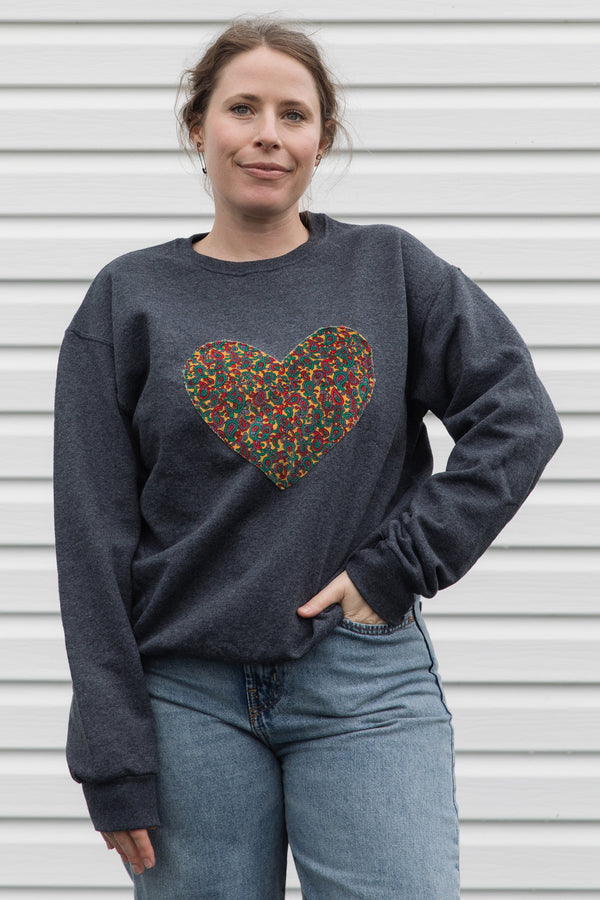 Woman wearing a dark gray sweatshirt with a colorful heart design sewn in canada