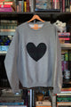 Woman wearing a unisex light grey sweatshirt with a navy, green plaid heart. 