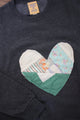 Dark gray sweatshirt with a heart-shaped patch featuring various fabrics on a wooden surface.
