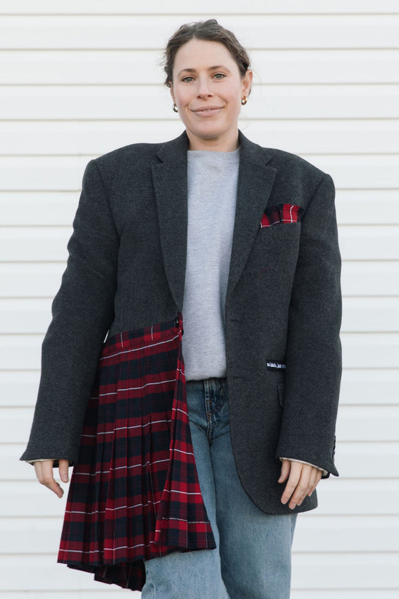 Person wearing a gray blazer, gray sweater, blue jeans, and a red plaid skirt against a white background.