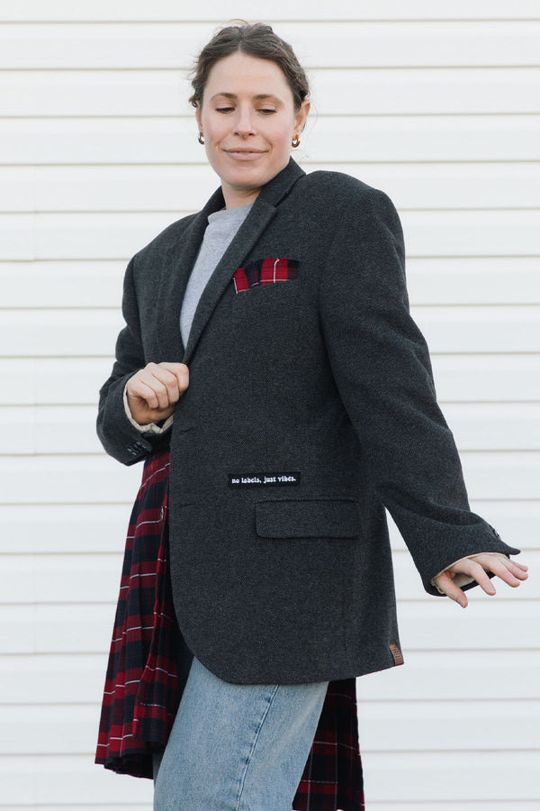 Person wearing a dark gray blazer with a red plaid pattern, standing against a white background.