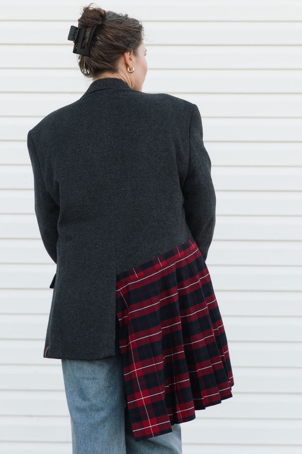 Person wearing a dark gray blazer over a red plaid skirt with blue jeans against a white background