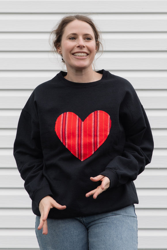 Person wearing a black sweatshirt with a red striped heart design 
