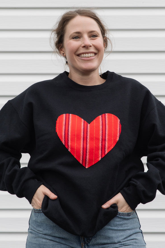 Person wearing a black sweatshirt with a red striped heart design 