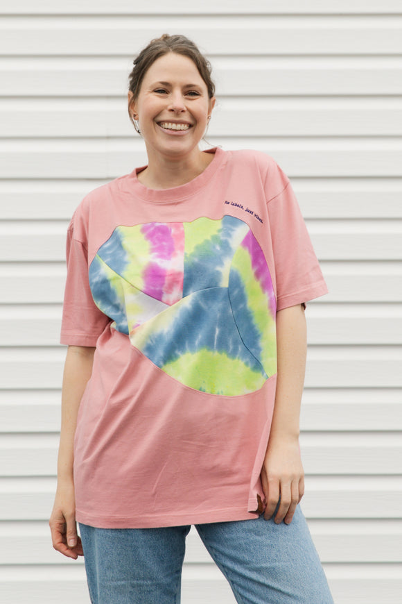 Person wearing a pink t-shirt with a colorful tie-dye design against a white background, upcycled in canada