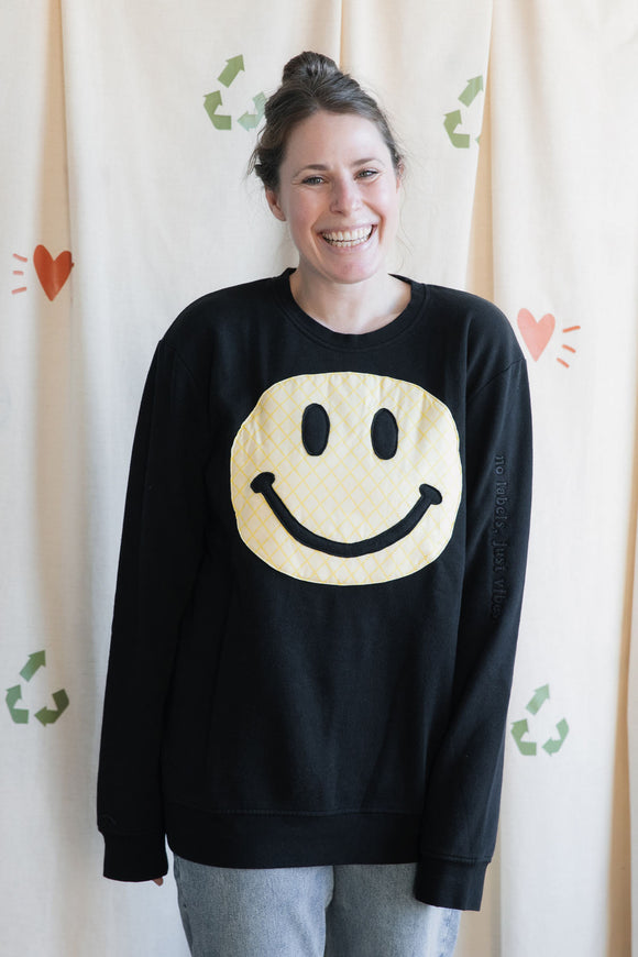 person wearing a black sweater with a quilted yellow smiley face, upcycled in canada