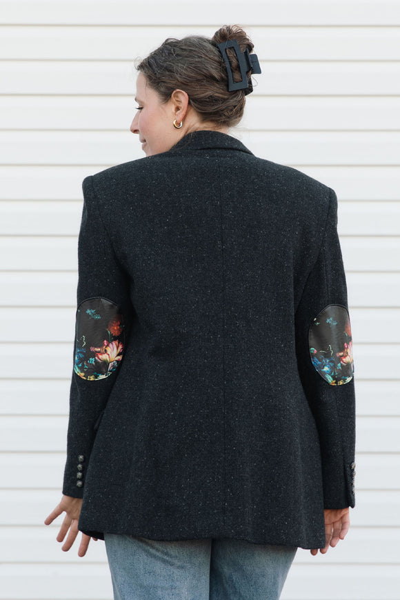Person wearing a black blazer with floral elbow patches against a white background