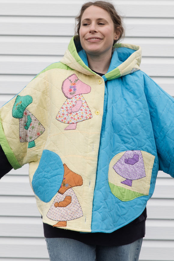 Person wearing a colorful quilted jacket with appliqué designs, featuring yellow, green and blue colours, upcycled in canada