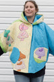 Person wearing a colorful quilted jacket with appliqué designs, featuring yellow, green and blue colours, upcycled in canada