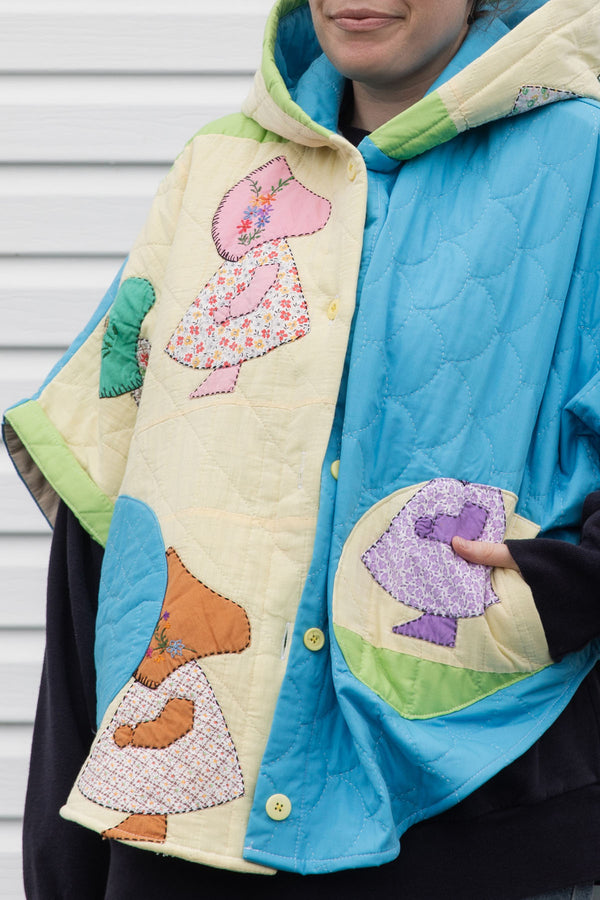 Person wearing a colorful quilted jacket with appliqué designs, featuring yellow, green and blue colours, upcycled in canada