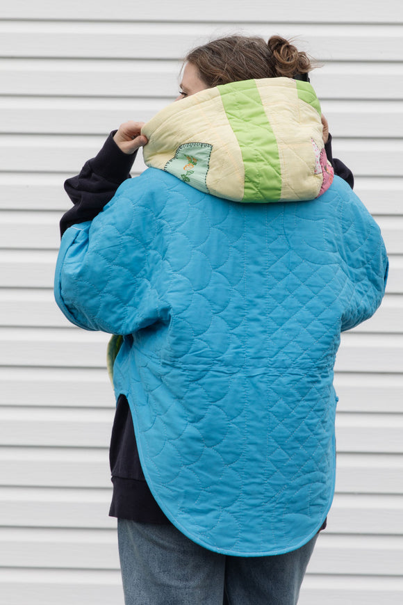 Person wearing a colorful quilted jacket with appliqué designs, featuring yellow, green and blue colours, upcycled in canada