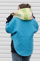 Person wearing a colorful quilted jacket with appliqué designs, featuring yellow, green and blue colours, upcycled in canada