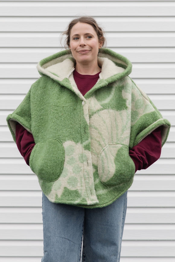 person wearing green wool poncho with oversized hood and fit, featuring pocket up and button up front, upcycled in canada