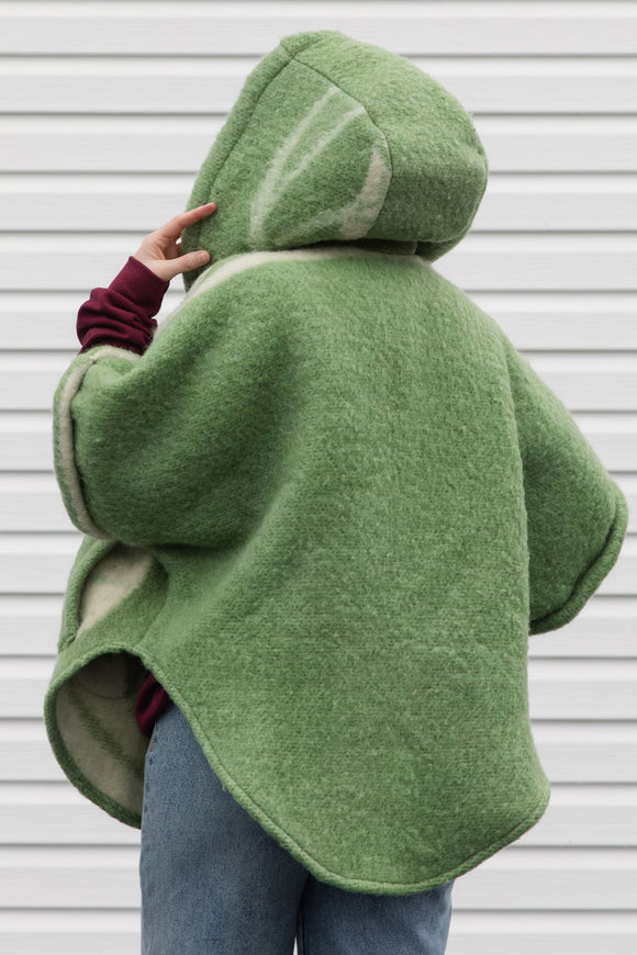person wearing green wool poncho with oversized hood and fit, featuring pocket up and button up front, upcycled in canada