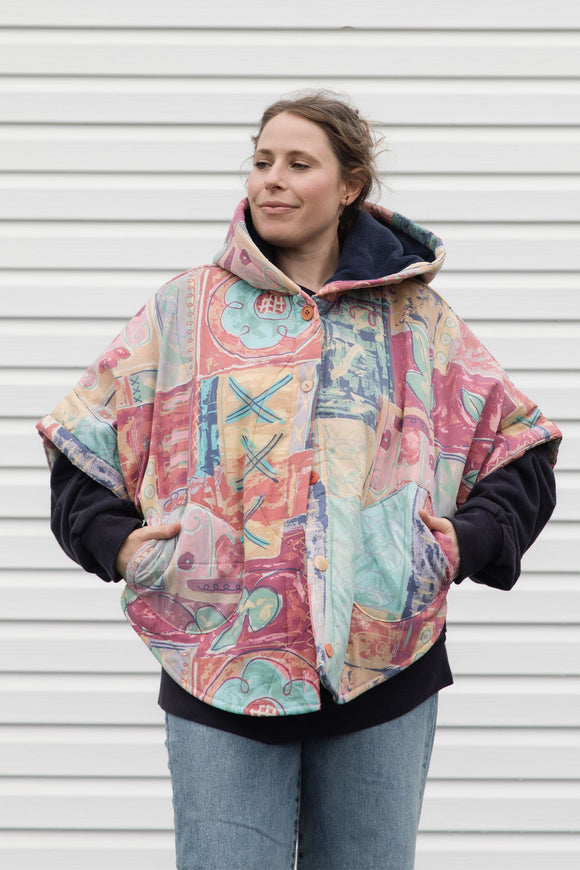 person wearing an oversized poncho, featuring a hood, pockets and button up front, upcycled from a pastel 90's comforter, made in canada
