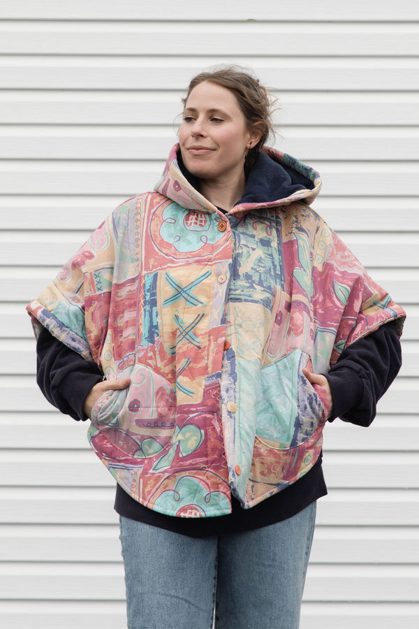 person wearing an oversized poncho, featuring a hood, pockets and button up front, upcycled from a pastel 90's comforter, made in canada