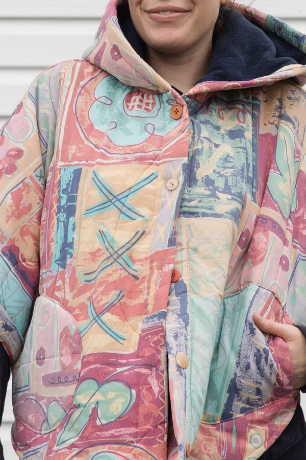 person wearing an oversized poncho, featuring a hood, pockets and button up front, upcycled from a pastel 90's comforter, made in canada