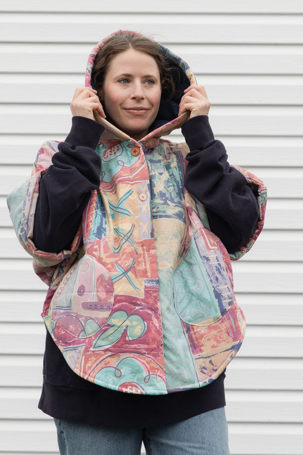 person wearing an oversized poncho, featuring a hood, pockets and button up front, upcycled from a pastel 90's comforter, made in canada