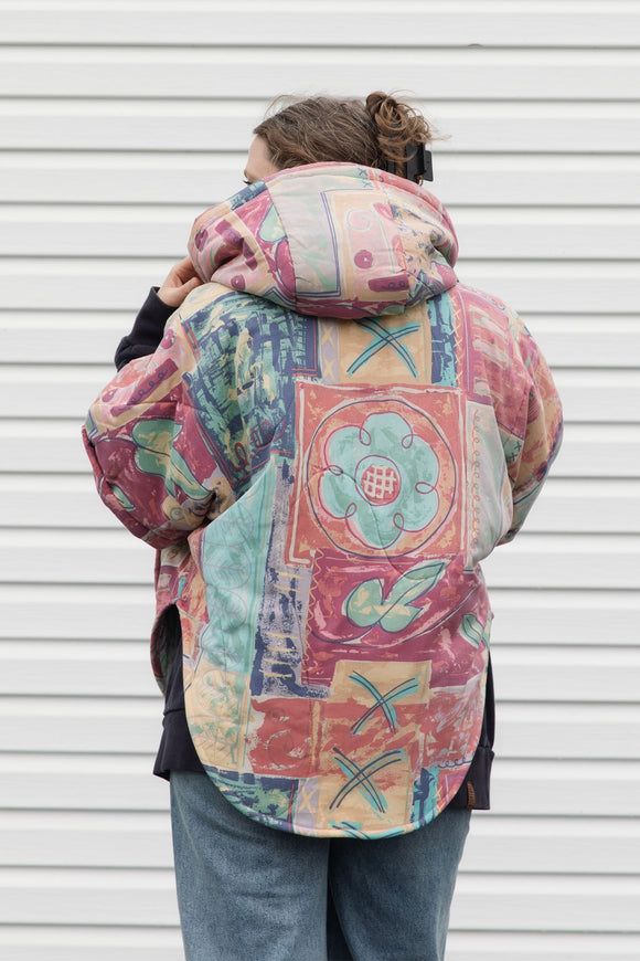 person wearing an oversized poncho, featuring a hood, pockets and button up front, upcycled from a pastel 90's comforter, made in canada