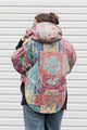 person wearing an oversized poncho, featuring a hood, pockets and button up front, upcycled from a pastel 90's comforter, made in canada