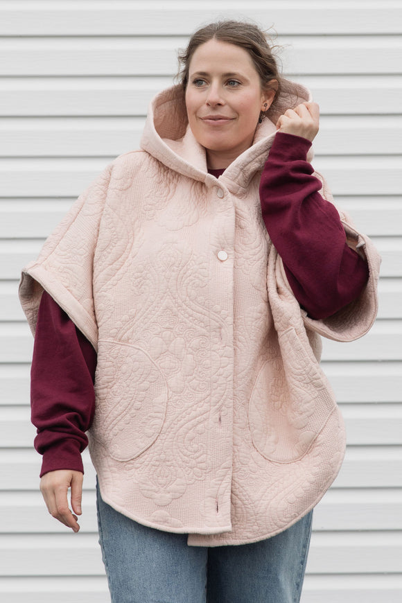 person wearing an oversized poncho with hood, pockets and button up front, upcycled from a pastel pink quilt