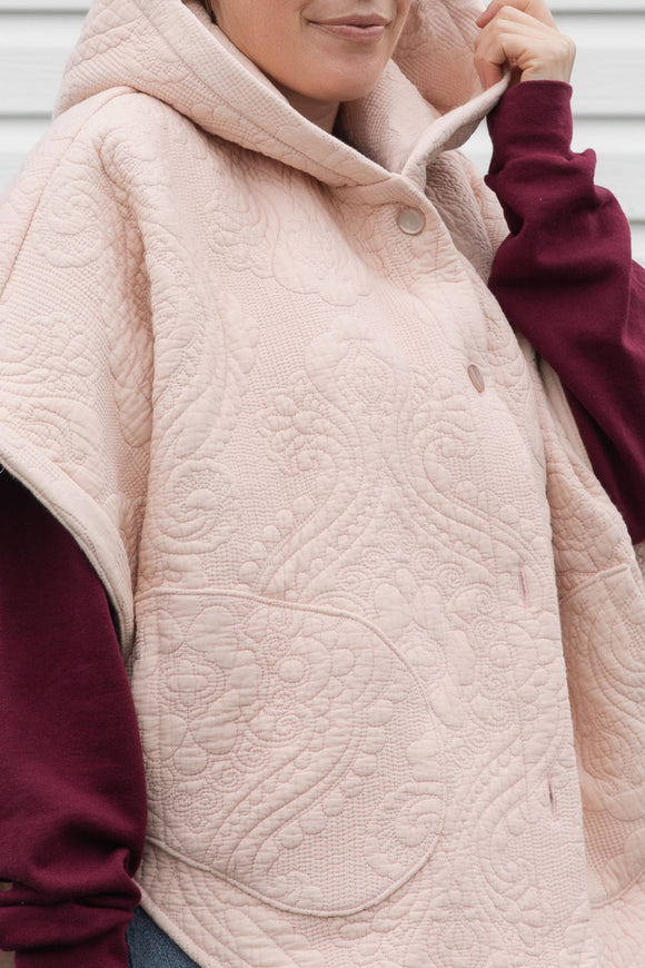 person wearing an oversized poncho with hood, pockets and button up front, upcycled from a pastel pink quilt