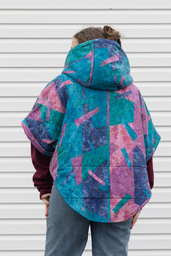 person wearing a colourful poncho jacket, featuring an oversized hood, pockets and a button up front, upcycled in canada