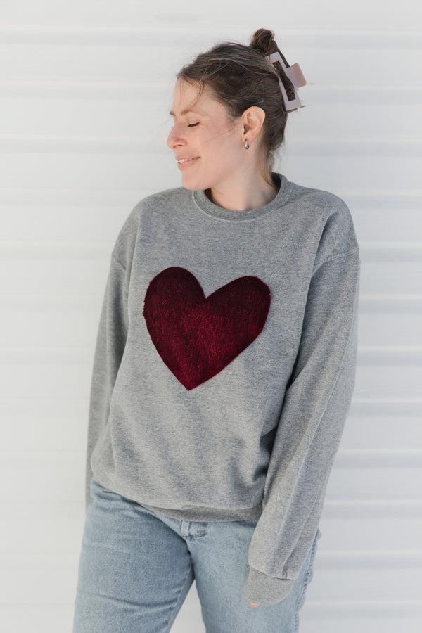 Person wearing a gray sweater with a red velvet heart design against a white background, sewn in canada