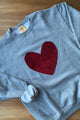 Person wearing a gray sweater with a red velvet heart design against a white background, sewn in canada