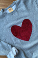 Person wearing a gray sweater with a red velvet heart design against a white background, sewn in canada